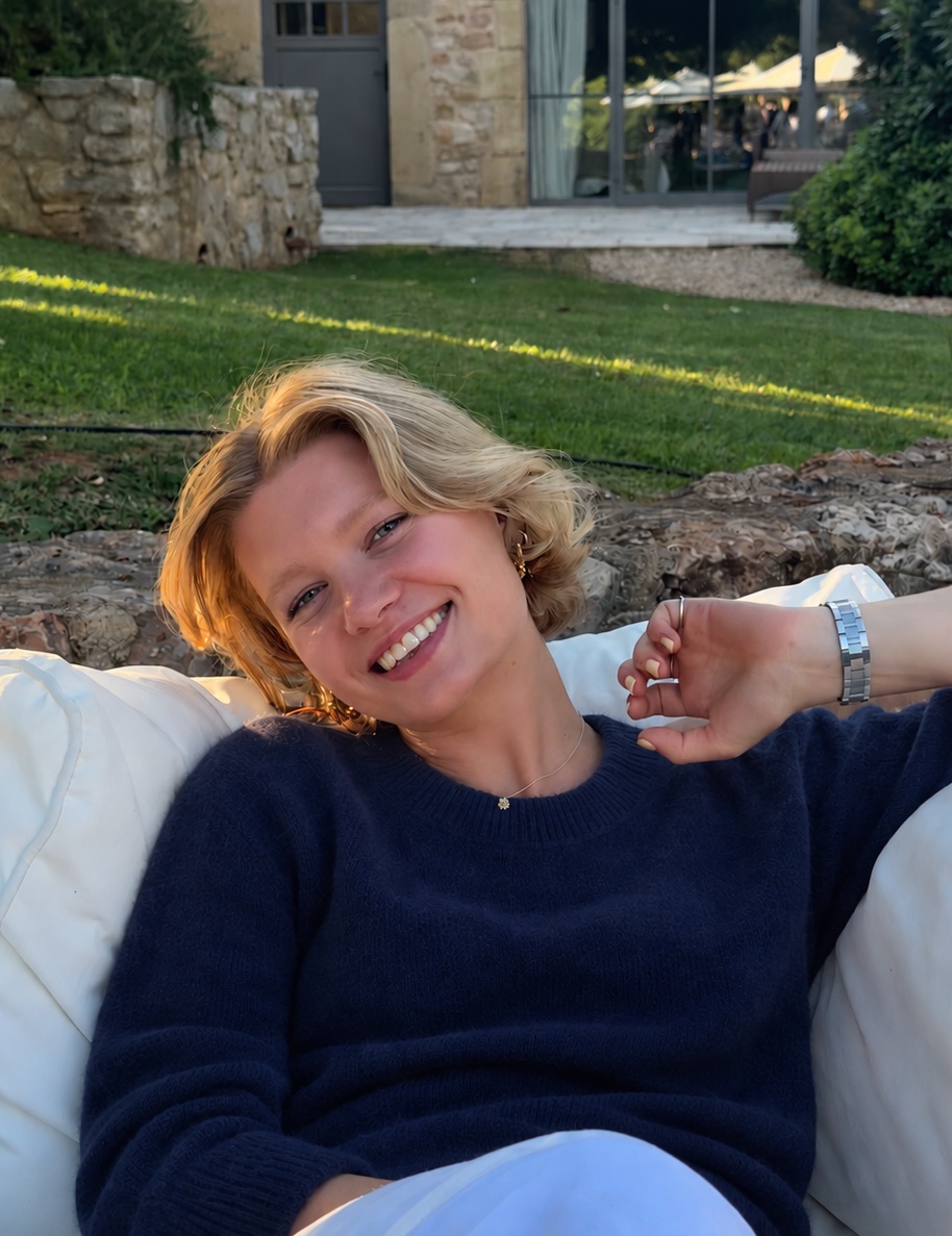 Kitty Berkeley, smiling, sitting outdoors on white cushions in a navy jumper.